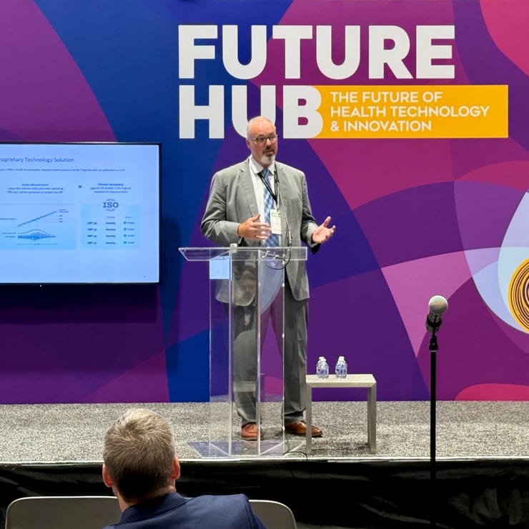 Omer Inan speaks from a clear lectern on the purple Future Hub stage, beside a screen showing a Biozen technology slide, with audience members in the foreground.