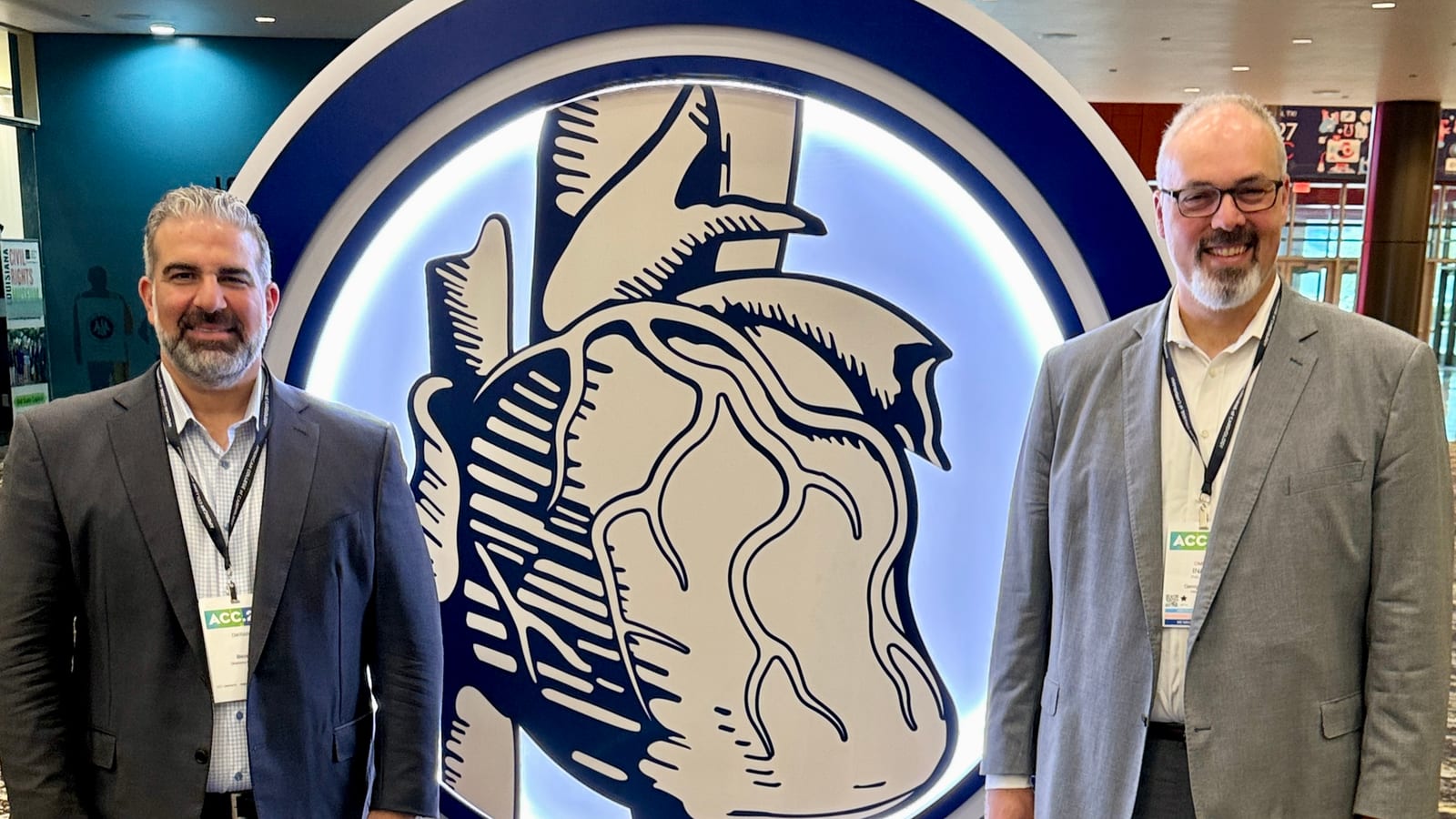 Dikran Tourian (left) and Omer Inan, PhD (right), in suits and ACC conference badges, stand on a blue carpet beside the illuminated American College of Cardiology heart emblem.