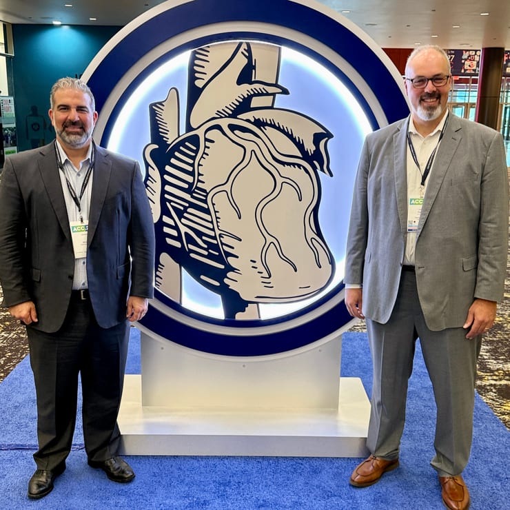 Dikran Tourian (left) and Omer Inan, PhD (right), in suits and ACC conference badges, stand on a blue carpet beside the illuminated American College of Cardiology heart emblem.